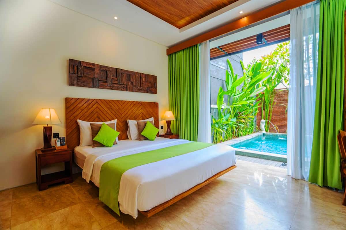 A hotel room with a large bed, wooden headboard, green curtains, and a view of a swimming pool.