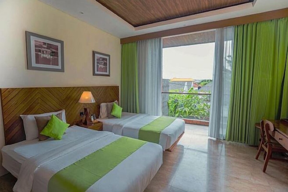 Habitación de hotel con dos camas, cabecera de madera, mesita de noche, lámpara y vistas al exterior por una puerta corredera.