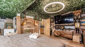 Een slaapkamer met een groot bed, een televisie en een wand versierd met planten en muziekinstrumenten.