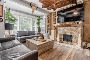 Un salon moderne avec une cheminée en pierre, des canapés en cuir et un téléviseur fixé au mur.