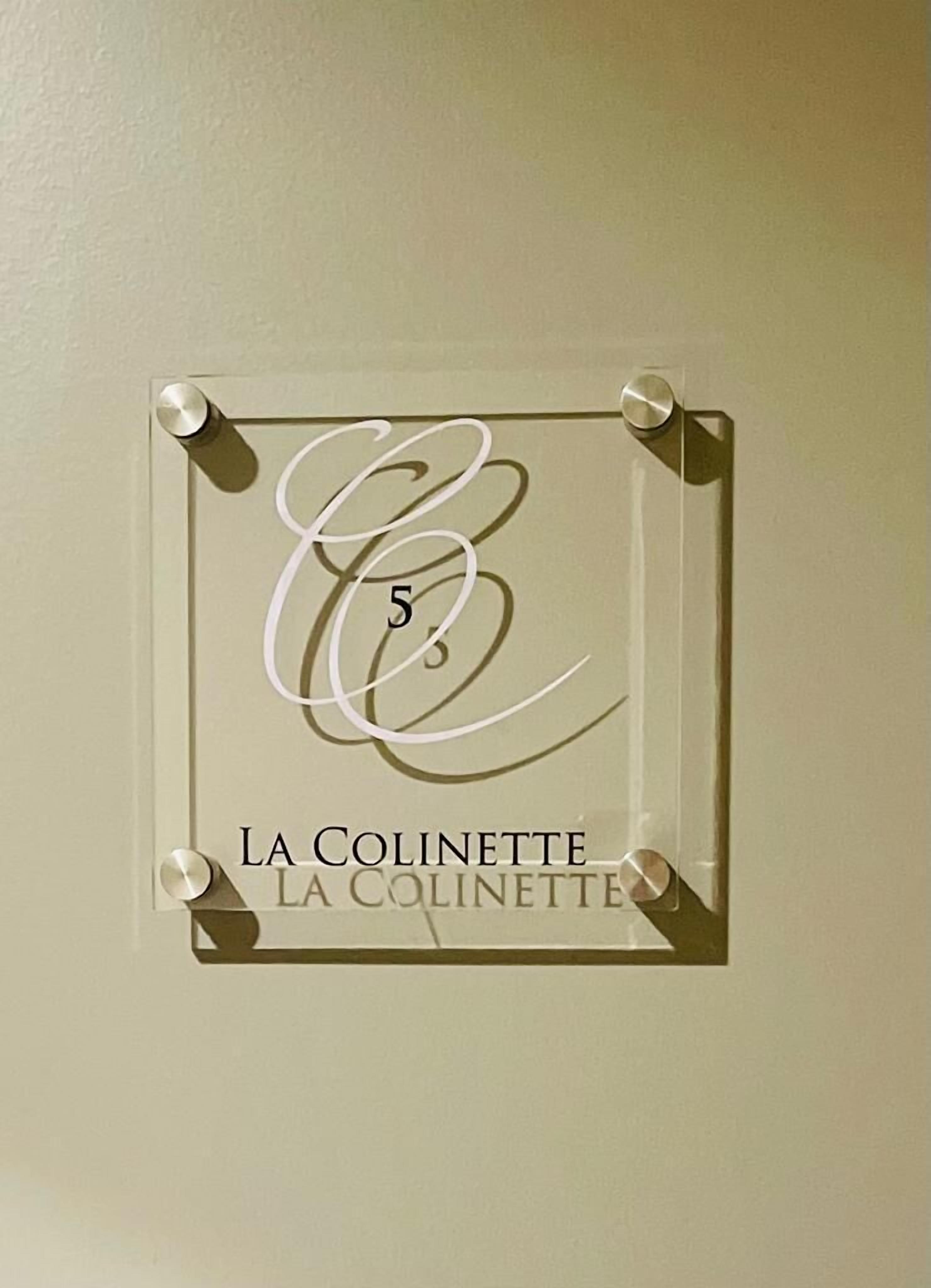 Une plaque encadrée, ornée d’un « E » stylisé et du chiffre « 5 », est fixée au mur. En dessous de la plaque, le texte « LA COLINETTE » est répété.