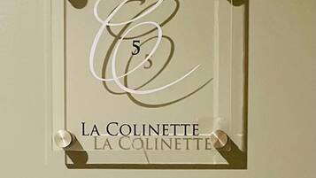 Une plaque encadrée, ornée d’un « E » stylisé et du chiffre « 5 », est fixée au mur. En dessous de la plaque, le texte « LA COLINETTE » est répété.