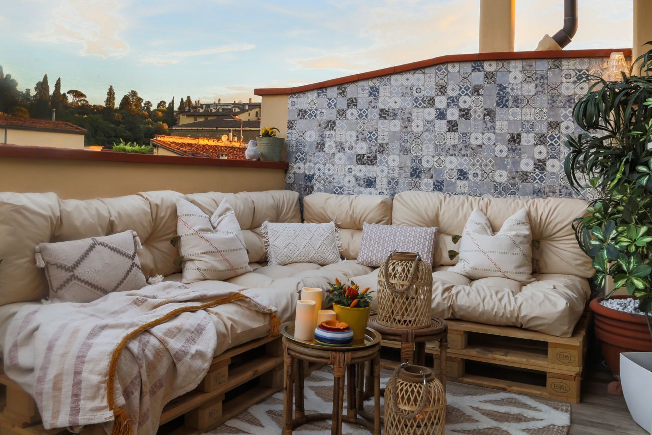 A cozy outdoor seating area with a cushioned sofa, wicker side tables, and a decorative wall.