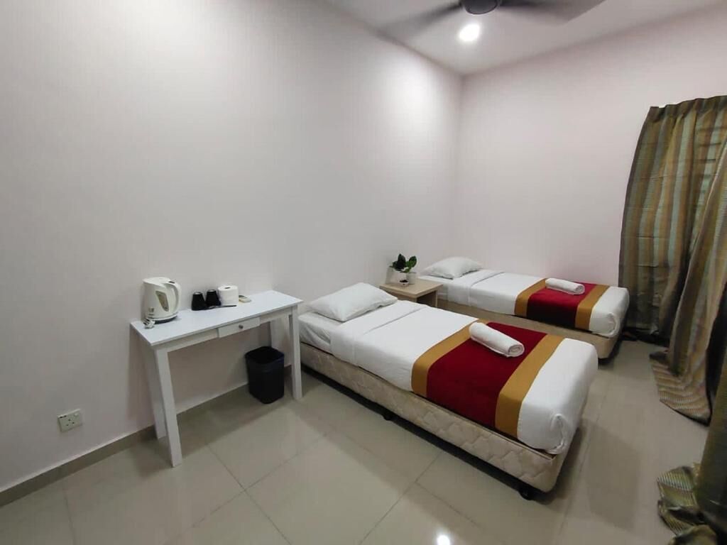 A hotel room with two beds, a desk, a chair, a trash bin, and a ceiling fan.