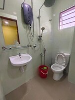A bathroom with a white sink, toilet, and shower. There is a red bucket on the floor.
