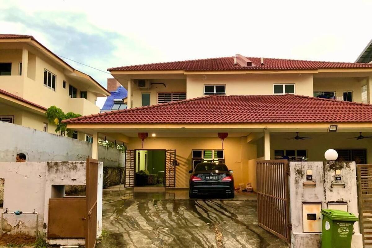 A two-story house with a red-tiled roof, a covered carport, and a gated entrance.