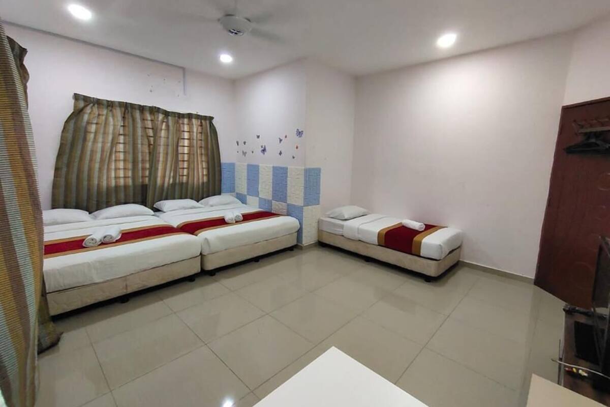 A hotel room with three beds arranged in a U-shape, a ceiling fan, and a tiled floor.