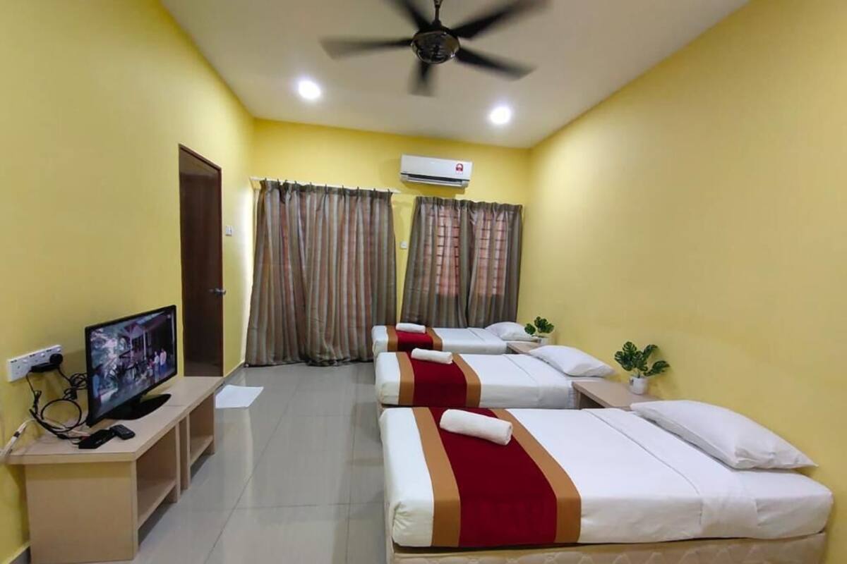 A hotel room with three beds, a TV, a desk, and an air conditioning unit.