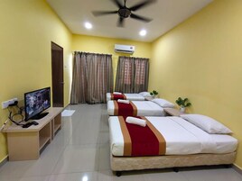 Habitación de hotel con tres camas, televisión, escritorio y aire acondicionado.