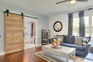 Uma sala de estar com uma porta deslizante rústica, um sofá com almofadas estampadas, uma mesa de centro com um arranjo floral e uma estante de livros.