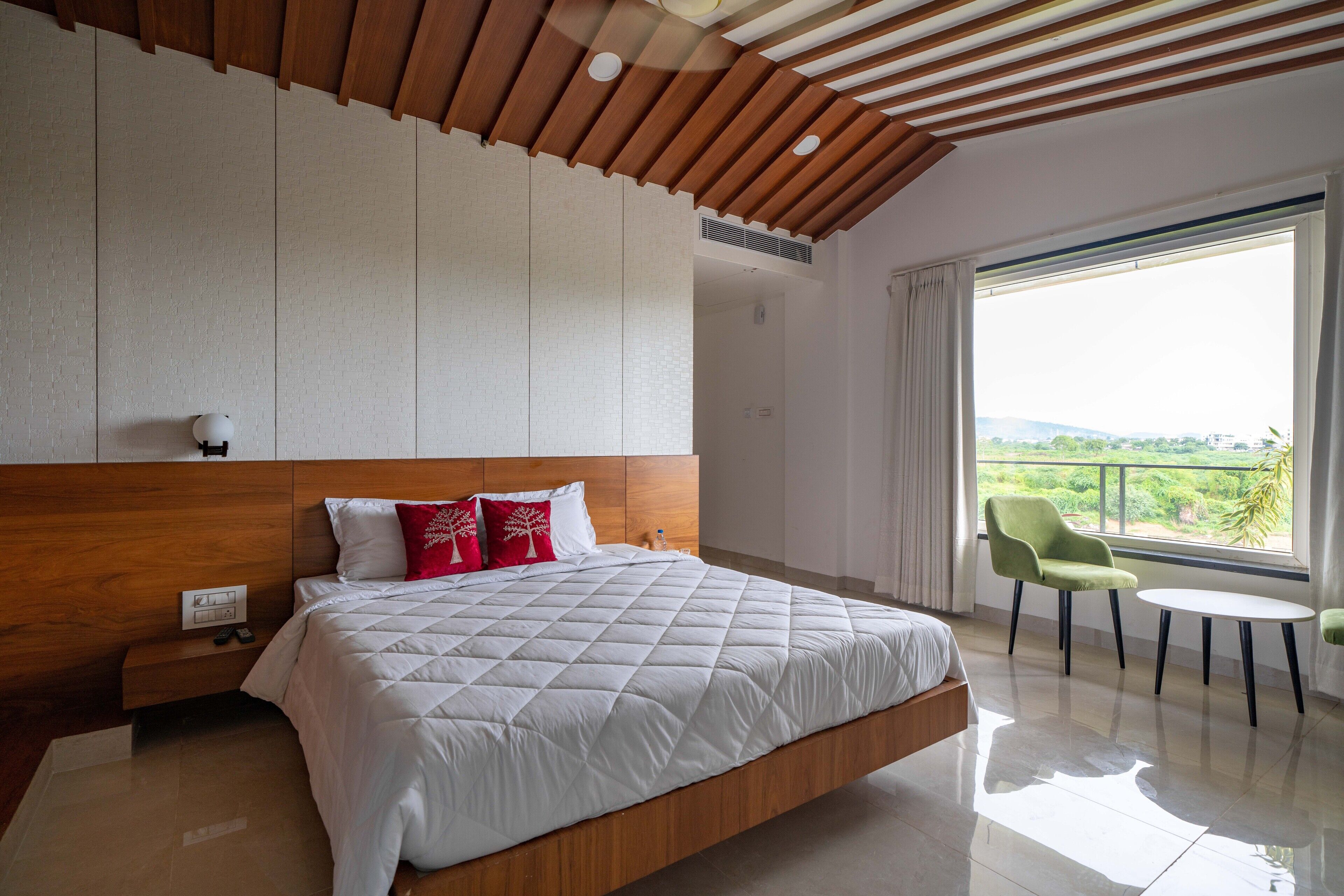 A modern hotel room with a large bed, a wooden ceiling, a balcony with a view, and a small table.