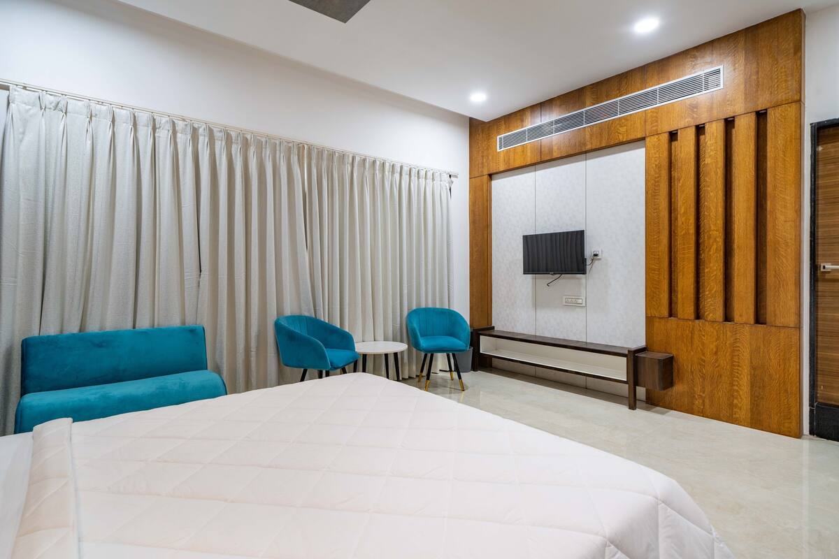 Hotelkamer met een groot bed, twee blauwe stoelen, een klein tafeltje, een televisie en een wand van hout.