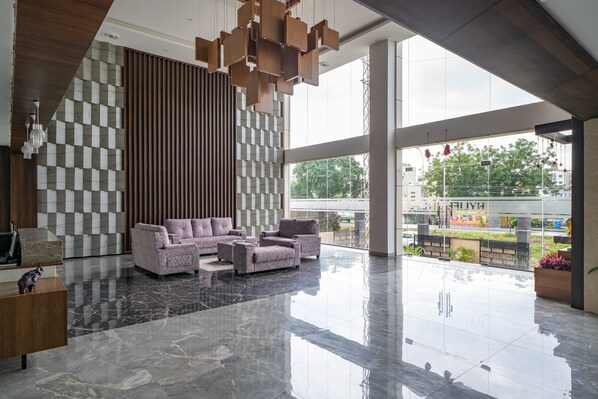 A modern lobby with a checkered wall, a seating area with sofas, and a large glass window offering a view of the outside.