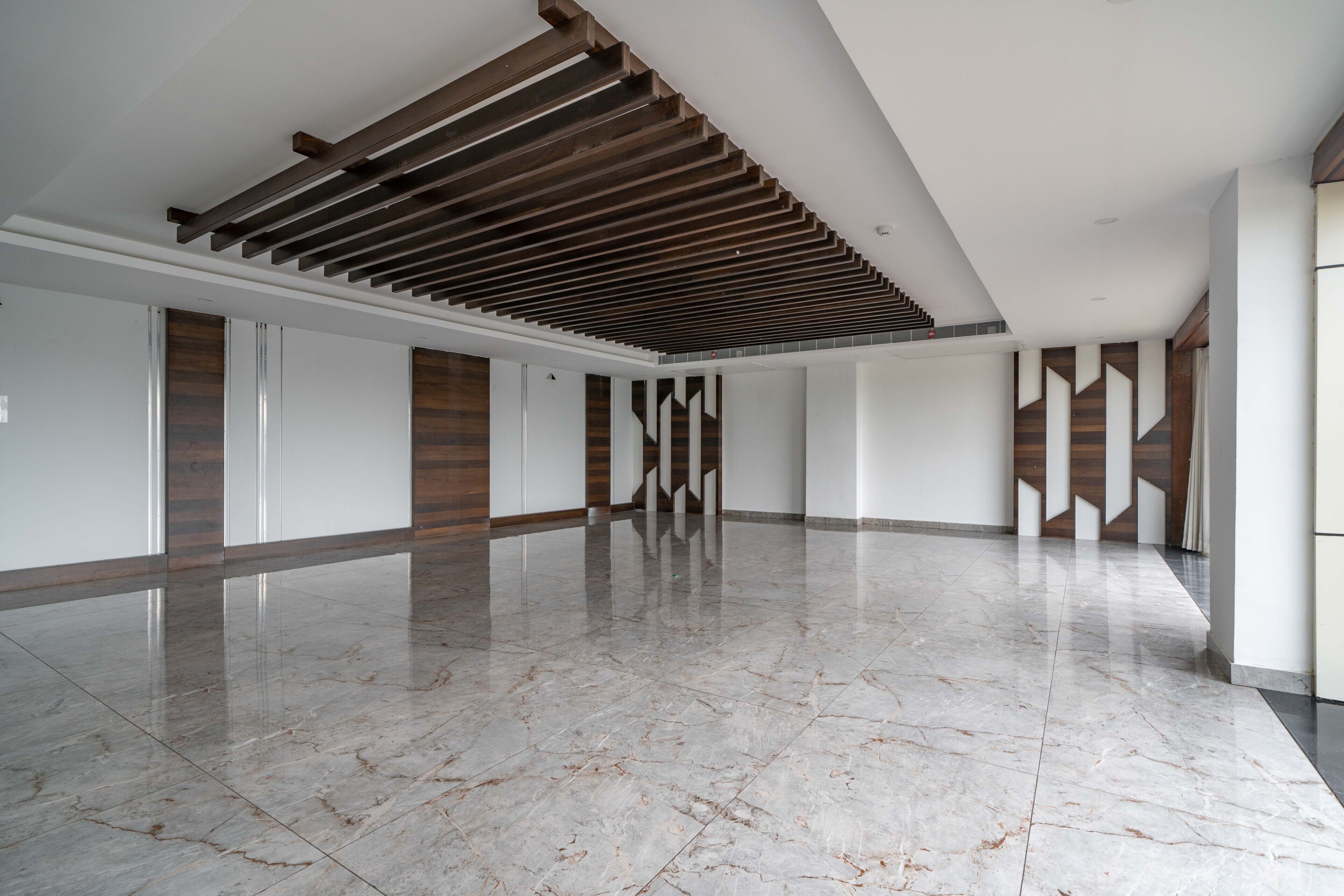 Un interior espacioso y moderno con piso de mármol pulido, detalles de paneles de madera y techo inclinado con vigas a la vista.