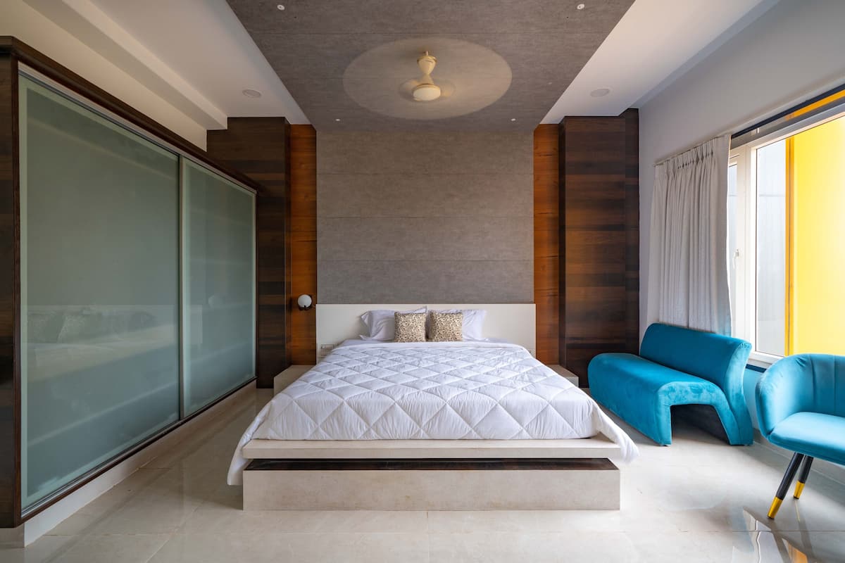 Een moderne slaapkamer met een groot bed, een blauwe stoel en een schuifdeur van glas.