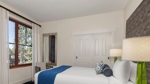 Ein Hotelzimmer mit Bett, Fenster mit Vorhängen, Spiegel, Tür und Lampe.