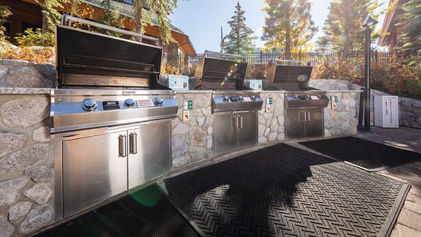 Une cuisine extérieure avec un mur en pierre, trois barbecues et un panneau d’avertissement concernant le gaz.