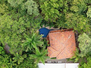 Eine Vogelperspektive zeigt ein Anwesen mit Swimmingpool, einem Ziegeldach und üppiger, umliegender Bepflanzung.