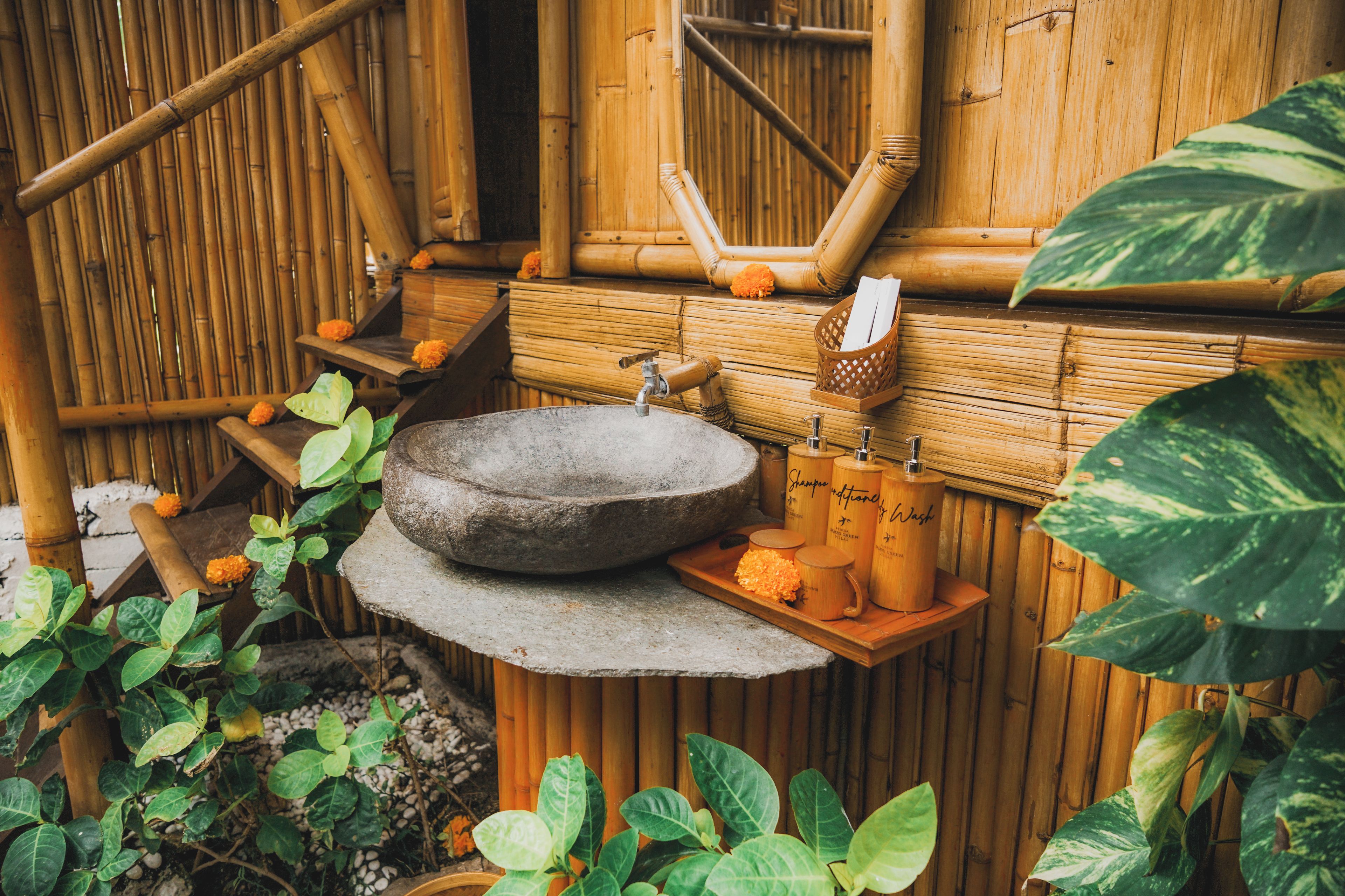 A traditional bamboo bathroom with a stone basin, wooden shelves, and a small wooden shelf with toiletries.