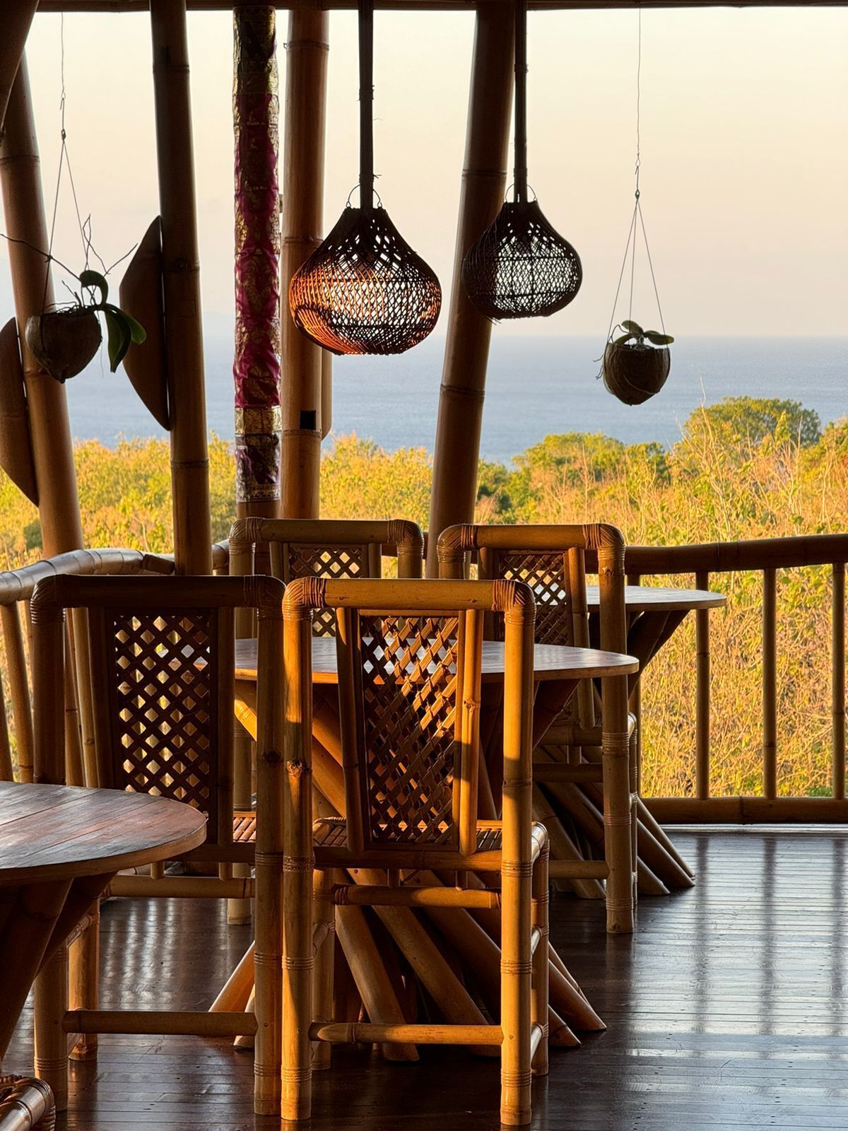 Un área de estar al aire libre decorada con bambú, con mesas y sillas, con vistas a un paisaje natural.