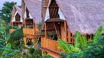 Un hotel in stile bungalow con tetti di paglia e balconi in legno, immerso in una rigogliosa vegetazione tropicale.