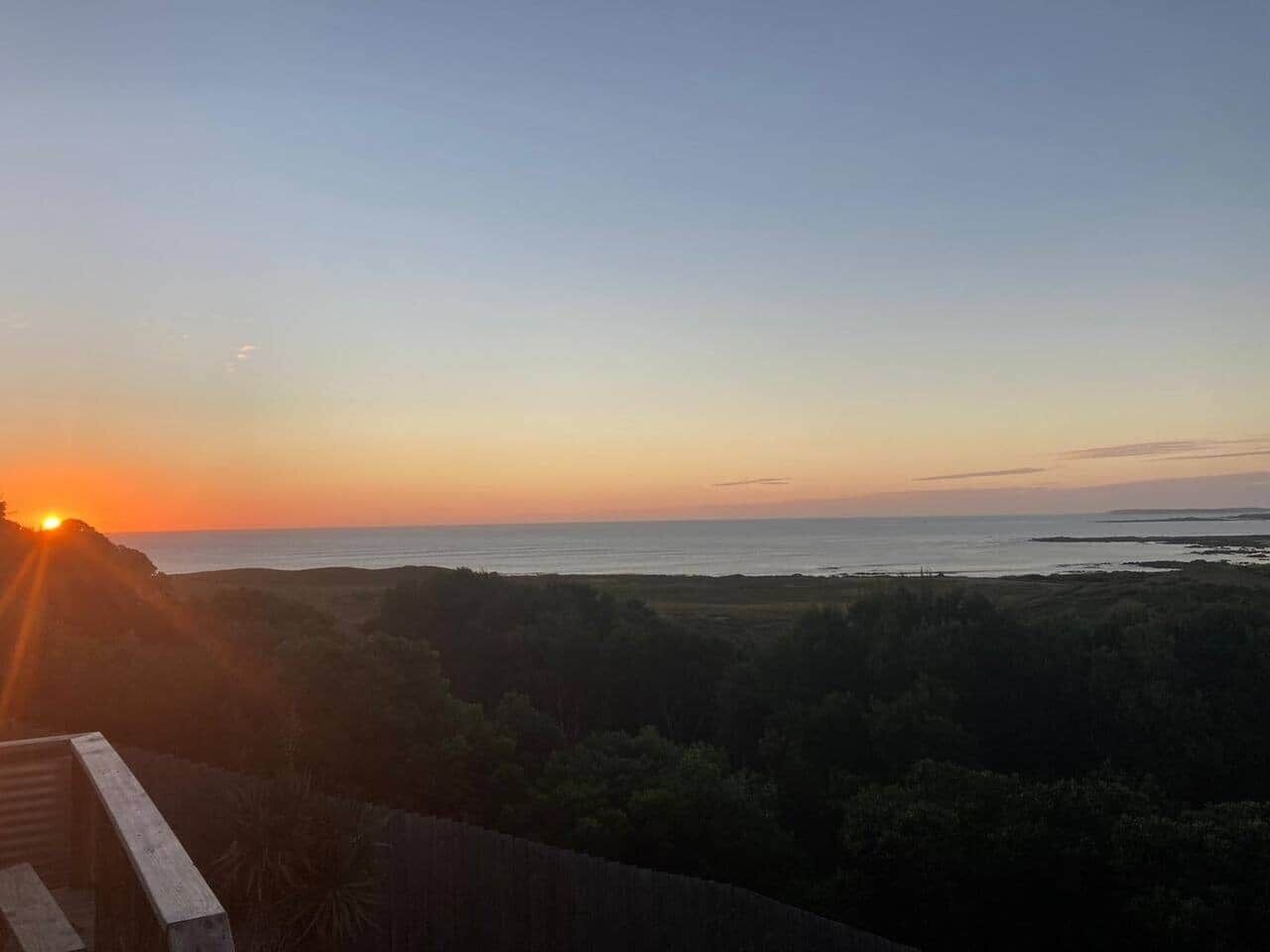 Une vue sur le coucher de soleil depuis un balcon donnant sur un paysage côtier.