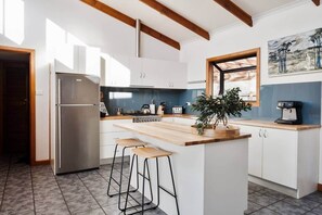 Une cuisine moderne dotée d’un îlot central, d’appareils électroménagers en acier inoxydable et offrant une vue sur l’extérieur.