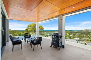 Relax on the spacious outdoor patio with a view of the surrounding landscape and distant water, featuring a comfortable seating area and outdoor cooking facilities.