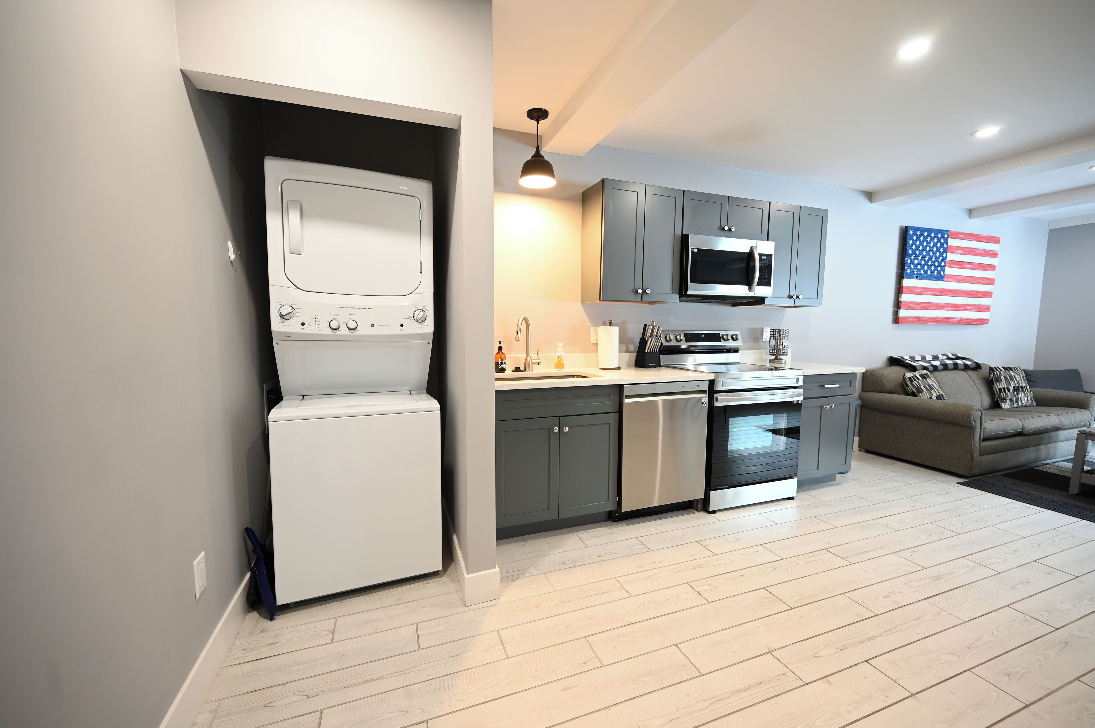 A modern kitchen with grey cabinets, stainless steel appliances, and a white washing machine.