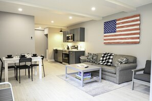 Ett modernt vardagsrum med en grå soffa, ett soffbord och en matplats med ett vitt bord och svarta stolar.