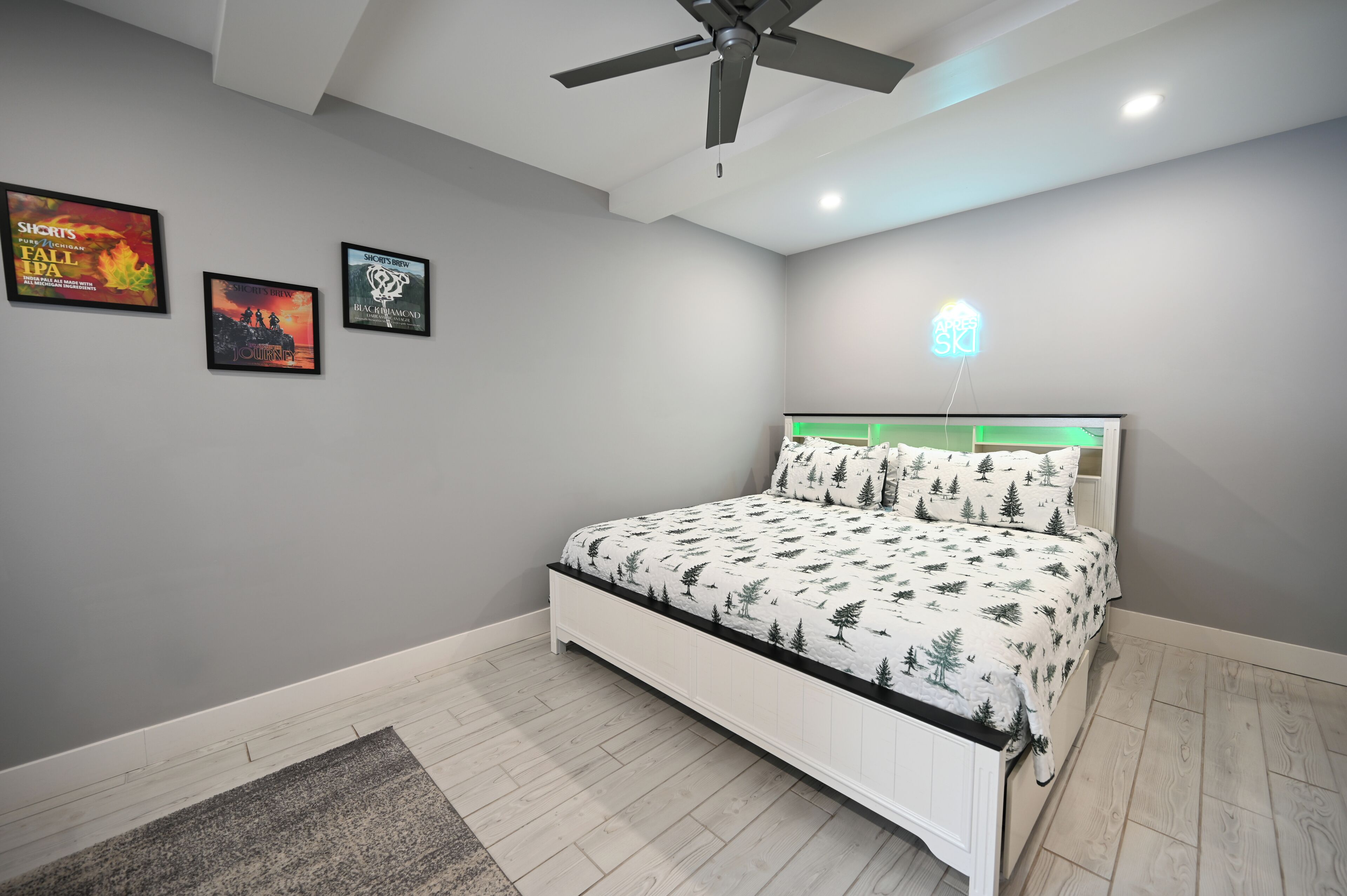 Une chambre à coucher avec un lit, un ventilateur de plafond et trois affiches encadrées accrochées au mur.