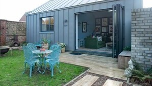 A modern building with a glass door entrance, a patio with metal chairs, and a brick wall. - Unique Boutique luxury Bed and Breakfast (Chichester)