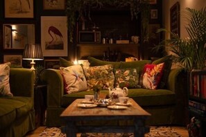 A cozy living room with a green sofa, a coffee table with decorative items, and a bookshelf filled with books and decorative objects. - Unique Boutique luxury Bed and Breakfast (Chichester)
