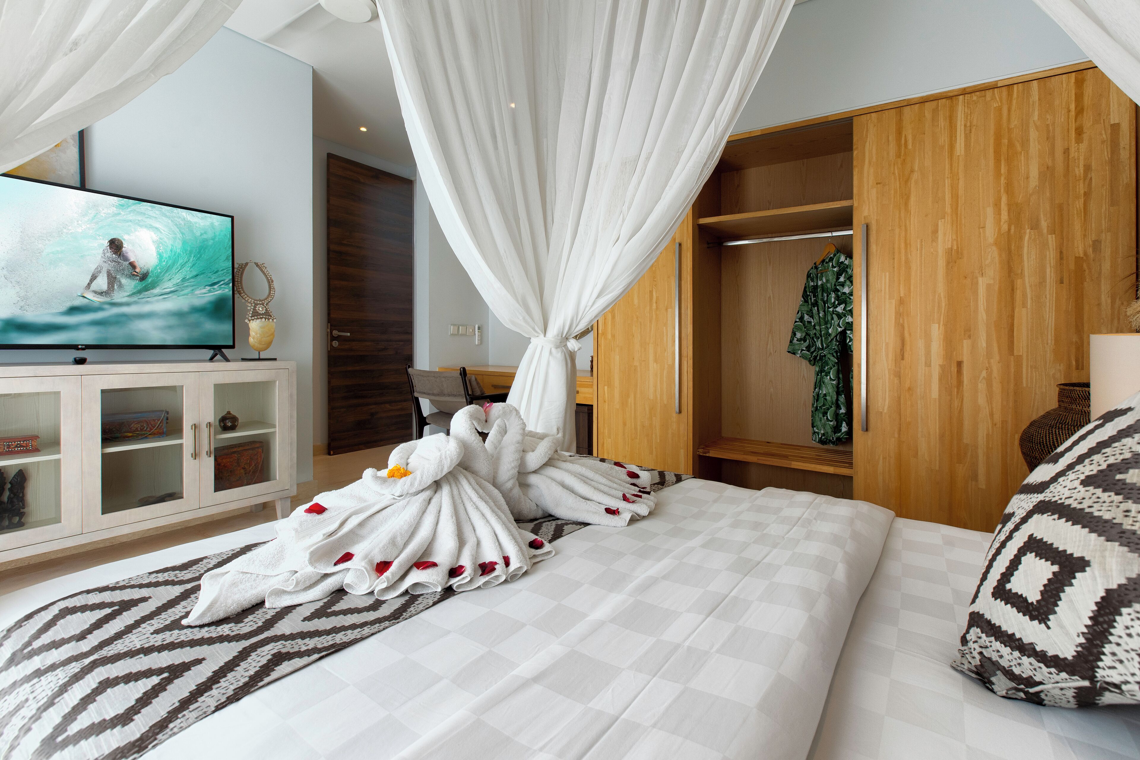A hotel room with a bed, a TV displaying a surfer, a wardrobe, and a bathroom with a shower curtain.
