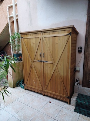 A wooden gate with a diagonal design, a potted plant, and a small figurine on the ground.