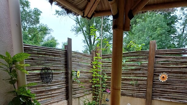 A covered outdoor seating area with wicker furniture, potted plants, and a bamboo fence. - 10-square-meter studio apartment + 18-square-meter terrace + Pool + Private parking  (Quissac)