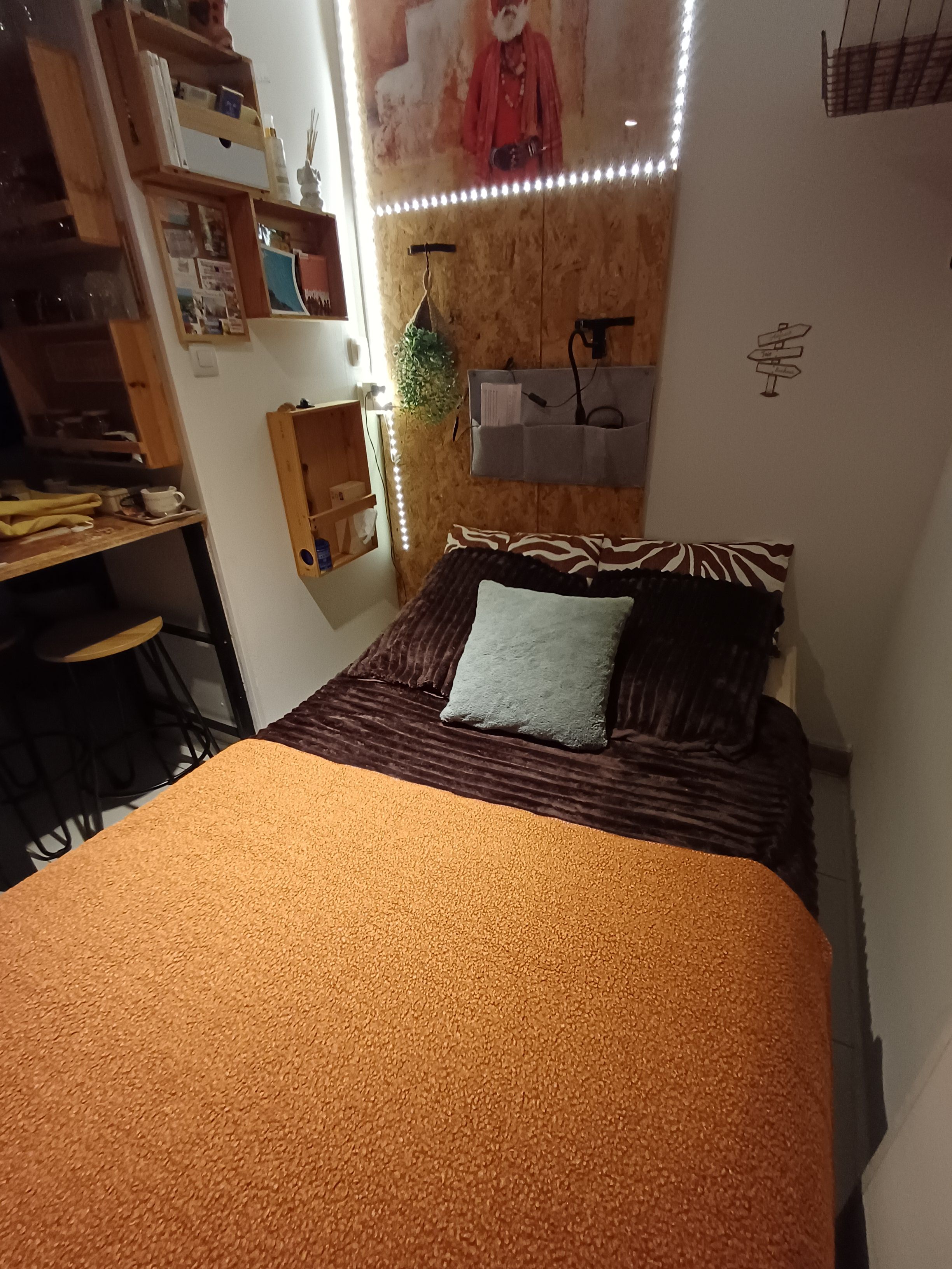 Een slaapkamer met een bed, een bureau en een plank met diverse spullen.