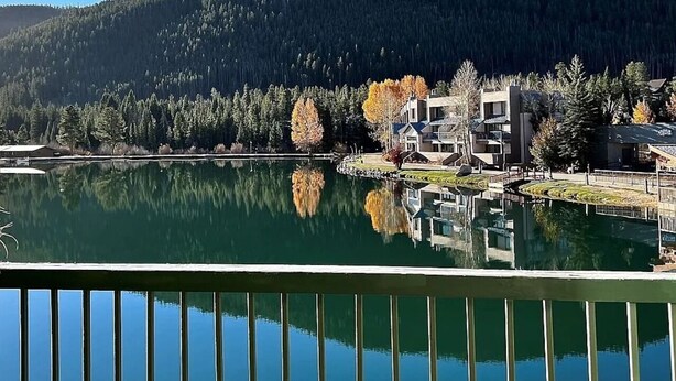 A lakeside view with buildings, a dock, and a forested mountain in the background. - Top-Floor Lake View Condo |P ool, Hot Tub, Shuttle (Keystone)
