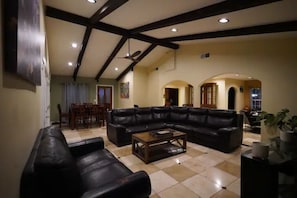 Uma sala de estar espaçosa com um amplo sofá de couro preto, uma mesa de centro de madeira e um espaço de jantar com mesa e cadeiras de madeira.