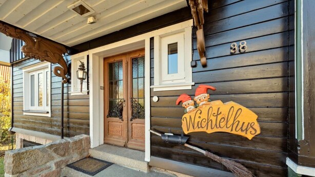 Una casa de madera con puerta principal, un porche y un letrero que dice 'Wichtelhaus'.