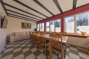 Un área de comedor con piso a cuadros, sillas de madera, una mesa, un sofá y ventanas grandes.