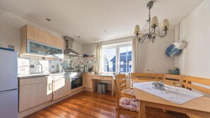 Una cocina con armarios de madera, una mesa de comedor con sillas, una lámpara de araña y un ventanal con cortinas.