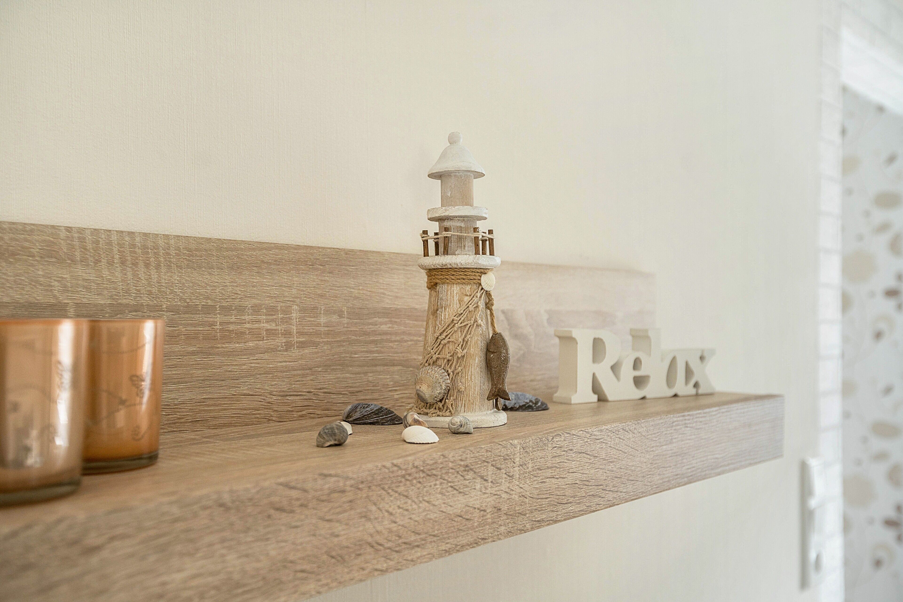 Ein Holzregal mit einem Leuchtturmmodell, Muscheln und einem Schild mit der Aufschrift 'Relax'.