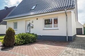 A modern two-story house with a tiled roof, a small garden, and a paved driveway. - Apartment "Kleiner Priel" with Wi-Fi (Wurster Nordseeküste)