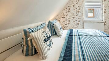Un dormitorio con techo inclinado, una ventana con persianas, ropa de cama a rayas y almohadas con motivos náuticos.
