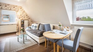 Una sala de estar acogedora con un sofá, una mesa de centro de cristal, una mesa de comedor con sillas, un radiador y una ventana con vistas.