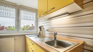 A kitchen with yellow cabinets, a stainless steel sink, a window with curtains, and a radiator.