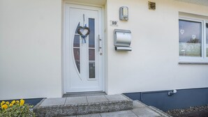 Una puerta blanca con un panel de vidrio, un letrero con el número '10', una luz adosada a la pared y una ventana decorada con corazones.
