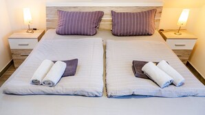 Ein Doppelbett mit zwei Kissen und zwei zusammengerollten Handtüchern, zwei Nachttische mit Lampen sowie ein Holz-Kopfteil.