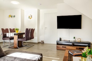 Una sala de estar moderna con comedor, televisor de pantalla plana montado en la pared y una mesa de centro de madera.